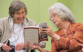 Dorothy Jessup and Lydia Stenzel, residents at Woodland Pond, joyfully examine Wartimes Remembered and remark on their contributions to the book.
