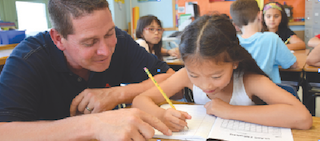 Dows Lane Elementary School teacher Christopher Cullen assists third-grader Ella Liu with a writing assignment on the first day of school on September 5.