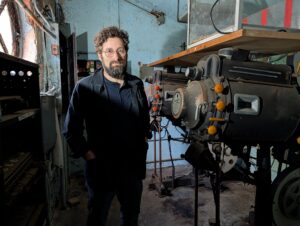 Lou Gruber stands next to a pair of vintage movie projectors tucked into a corner room in The Strand’s upper floor, on May 7, 2026. Photo: Robert Brum